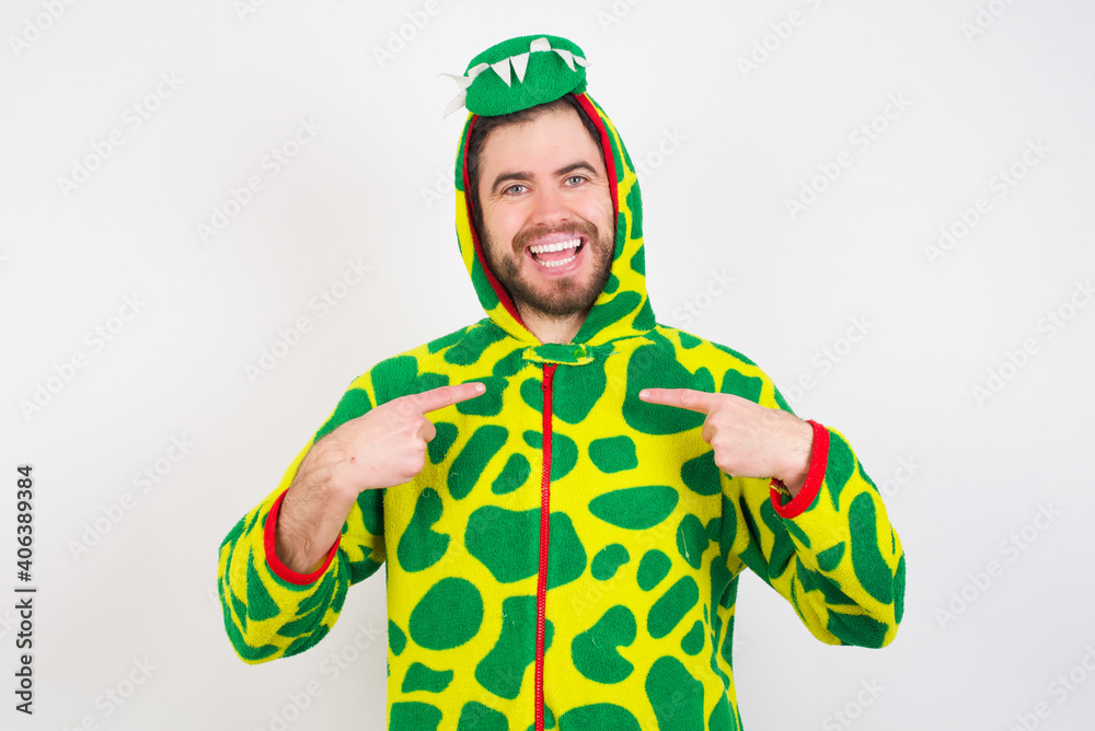 Fototapeta premium Young caucasian man wearing a pajama standing against white background points at his body, being in good mood after going shopping and making successful purchases