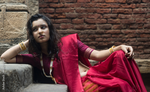 Portrait of beautiful Indian girl in heritage stepwell wearing traditional Indian red saree, gold jewellery and bangles holding religious plate. Maa Durga agomoni shoot concept photo