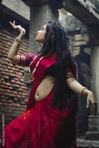 Portrait of beautiful Indian girl in heritage stepwell wearing traditional Indian red saree, gold jewellery and bangles holding religious plate. Maa Durga agomoni shoot concept photo