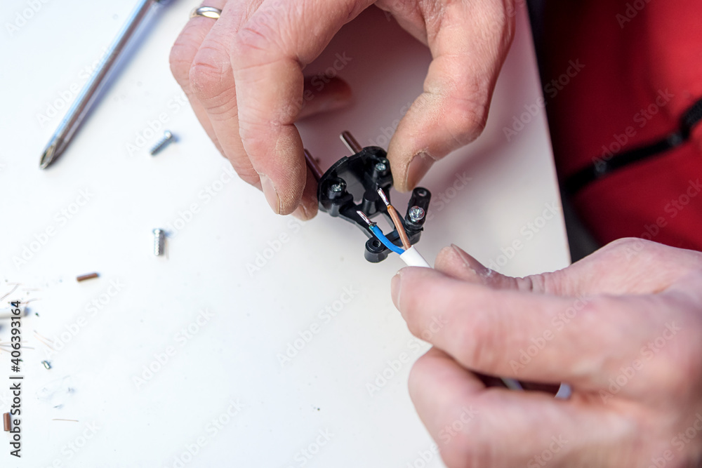 Fototapeta premium Close-up on the hands of a Caucasian electrician holding a screwdriver, working on the plug of an electrician on a white background. Collecting the socket.