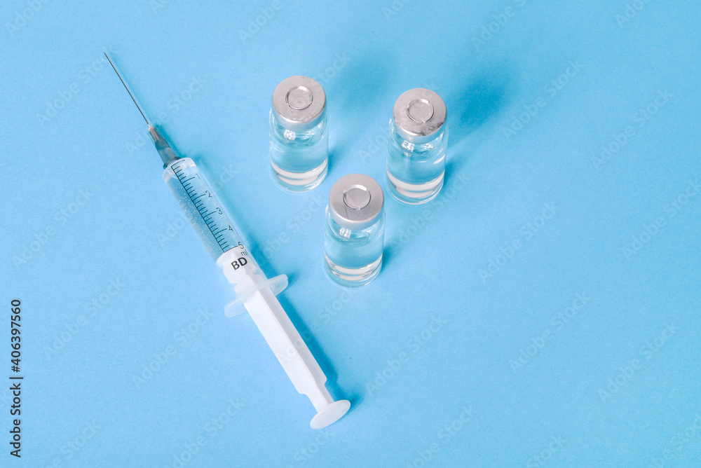 COVID-19 vaccine on a blue background. Vaccine vial for coronavirus treatment. Corona virus treatment concept, injection. Vaccine trials during a pandemic COVID-19 vaccine on a blue background. Vaccine vial for coronavirus treatment. Corona virus treatment concept, injection. Vaccine trials during a pandemic