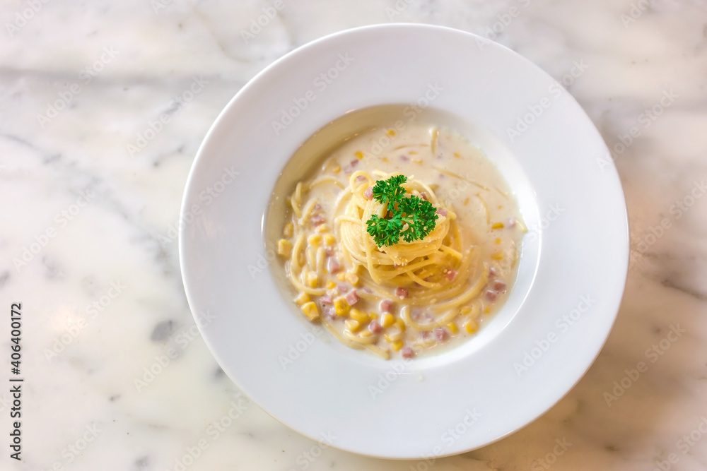 Spaghetti with ham and corn cream sauce put on a white plate on marble table as a background. Spaghetti with ham and corn cream sauce put on a white plate on marble table as a background.