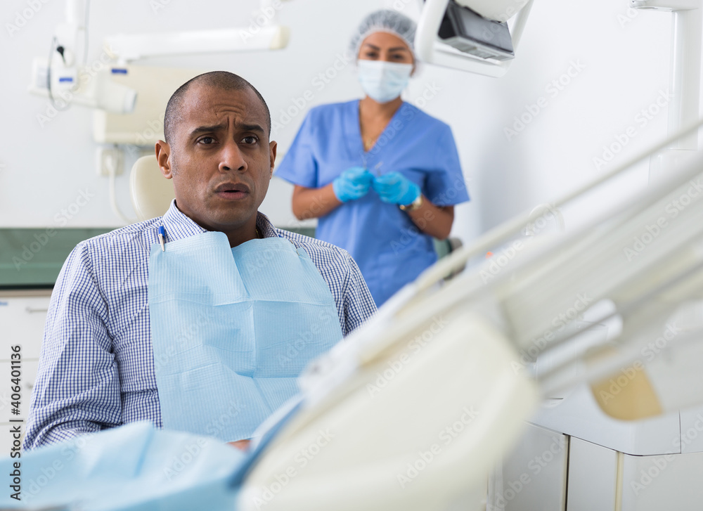 Obraz premium Portrait of scared Latin American sitting on dental chair waiting for treatment procedures in dentist office