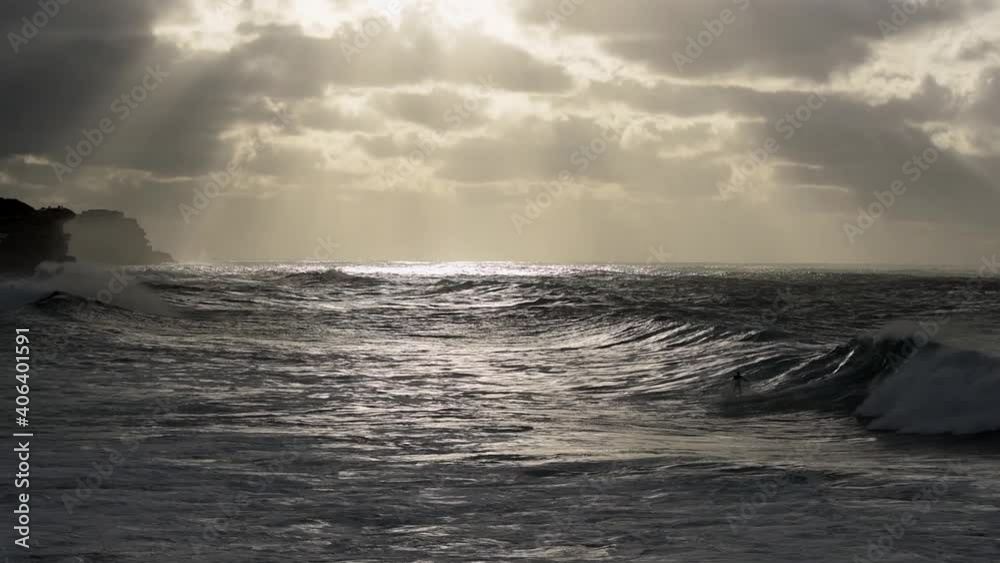 Unrecognisable lone surfer riding wave from right to left of screen during stormy sunrise at Bronte Beach Sydney Unrecognisable lone surfer riding wave from right to left of screen during stormy sunrise at Bronte Beach Sydney