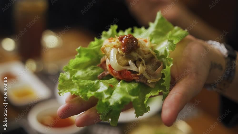 Hand With Ssam - Korean Pork Belly Wrapped In Lettuce Leaf With Ssamjang And Onions. - close up shot