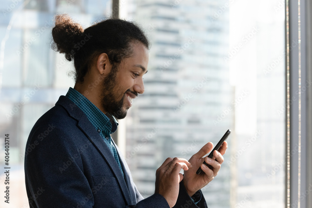 Smiling African American man look at smartphone screen browse surf wireless internet on modern gadget. Happy ethnic biracial businessman use cellphone consult client online, text or message on device. Smiling African American man look at smartphone screen browse surf wireless internet on modern gadget. Happy ethnic biracial businessman use cellphone consult client online, text or message on device.
