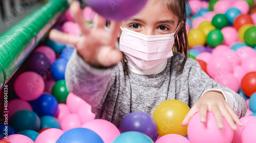 happy 5 year old girl with mask in a ball pool throwing balls to camera photo