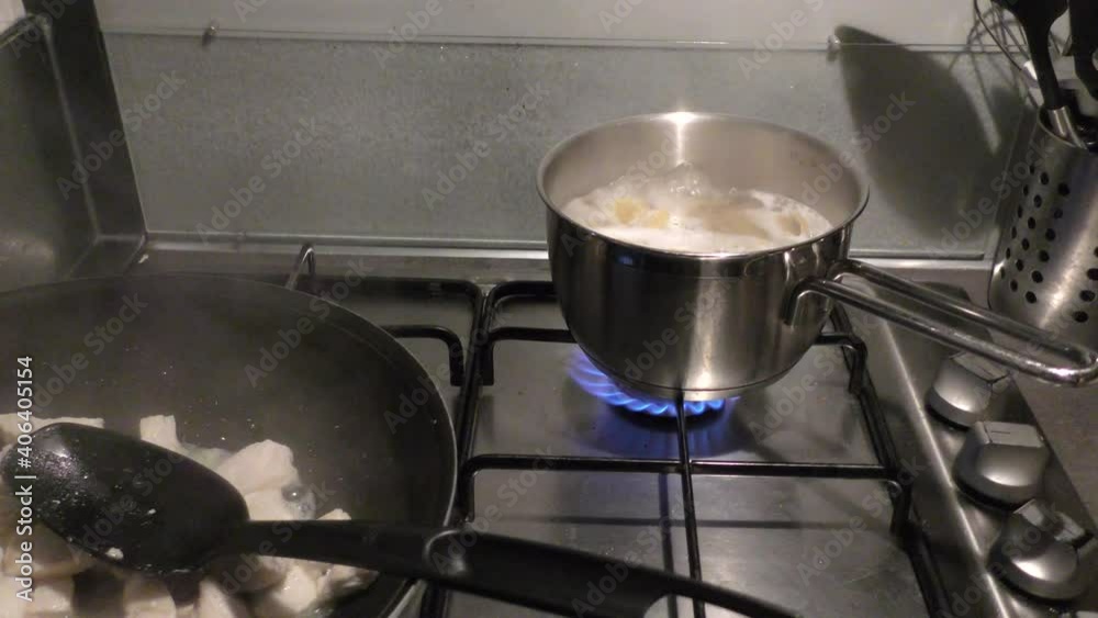 Pasta boiling in a pot and chicken meat frying in pan on stove top. Pasta boiling in a pot and chicken meat frying in pan on stove top.