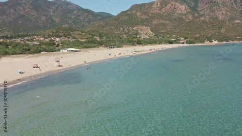 Fly Drone Slide View of Tropical Sea with People and Umbrellas at Beach. Mountains on Background. Tertenia, Sardinia, Italy photo