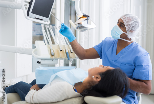 Qualified hispanic dentist pointing at teeth x-ray image on computer monitor explaining future treatment to female patient in dental clinic