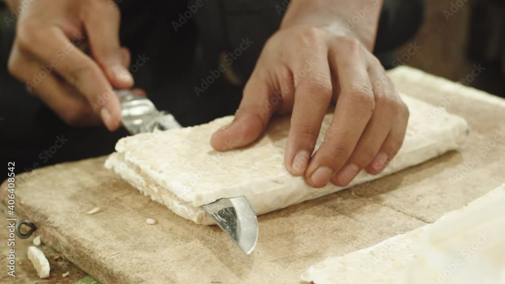 Close up shot of vendor cutting traditional raw tempe into slices. Tempe is a traditional Indonesian soy product, that is made from fermented soybeans. Close up shot of vendor cutting traditional raw tempe into slices. Tempe is a traditional Indonesian soy product, that is made from fermented soybeans.
