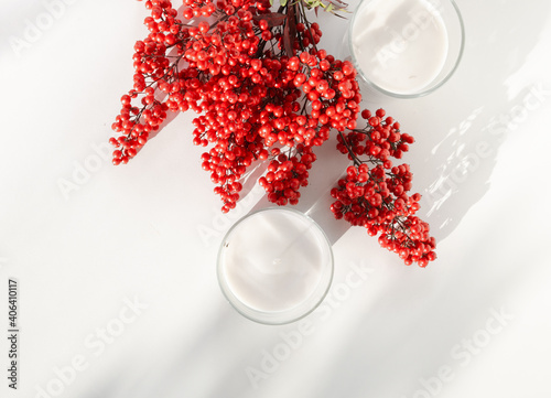 Two white candles with a red flower and berries