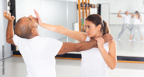 Obraz na płótnie Focused young Latina practicing basic self-defense techniques while training in gym with male partner, performing palm heel strike in chin