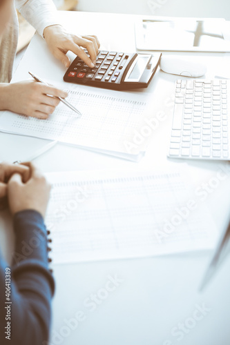 Accountant checking financial statement or counting by calculator income for tax form, hands close-up. Business woman sitting and working with colleague at the desk in office. Audit concept