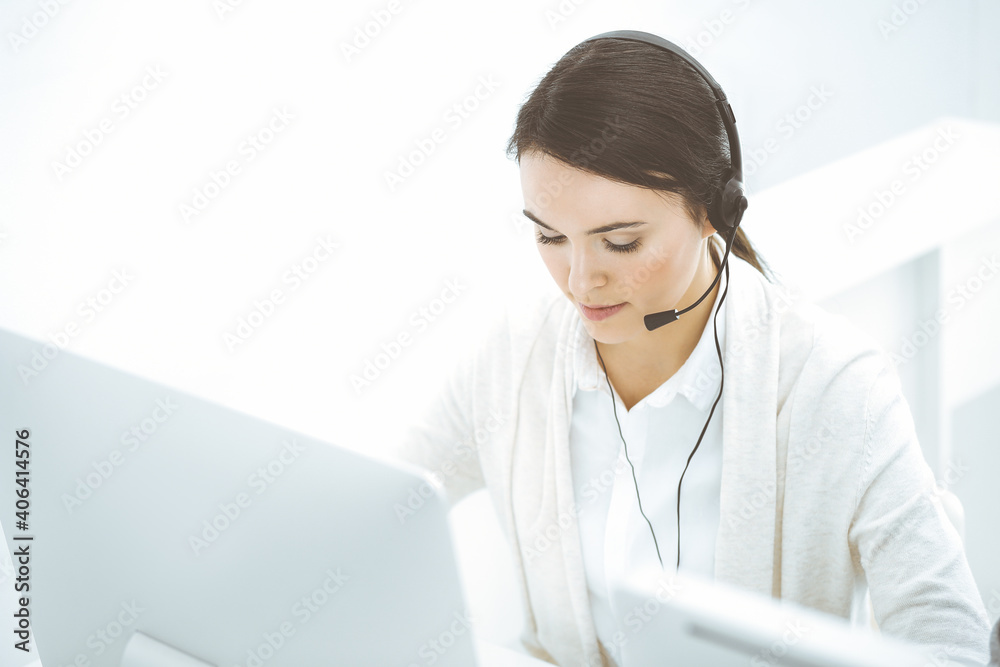 Call center. Casual dressed woman sitting and working in headset at customer service office. Business concept