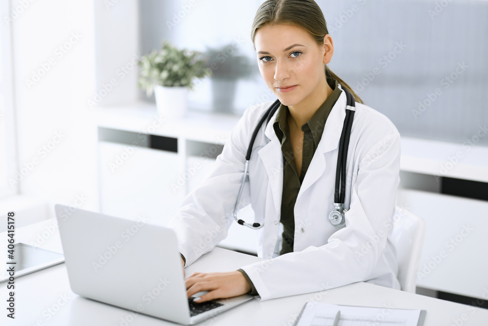Woman-doctor typing on laptop computer while sitting at the desk in hospital office. Physician at work. Data in medicine and healthcare Woman-doctor typing on laptop computer while sitting at the desk in hospital office. Physician at work. Data in medicine and healthcare
