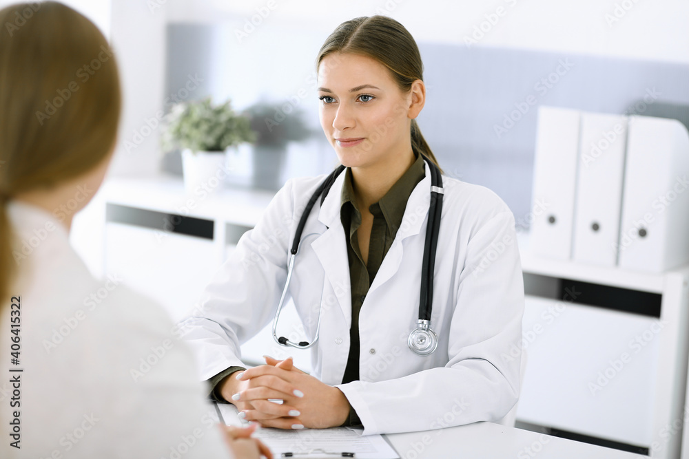Woman-doctor and patient sitting and talking at hospital office. Green color blouse suits to therapist. Medicine and healthcare concept Woman-doctor and patient sitting and talking at hospital office. Green color blouse suits to therapist. Medicine and healthcare concept