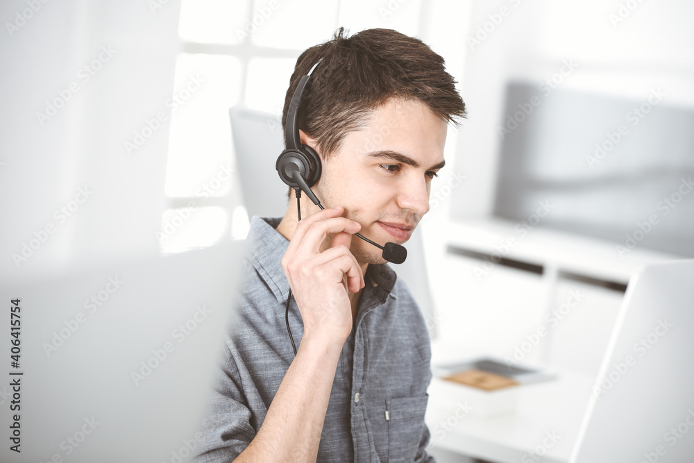 Casual dressed young man using headset and computer while talking with customers online. Call center, business concept Casual dressed young man using headset and computer while talking with customers online. Call center, business concept