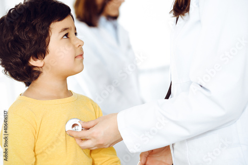 Woman-doctor examining a child patient by stethoscope. Cute arab boy at physician appointment. Medicine help concept