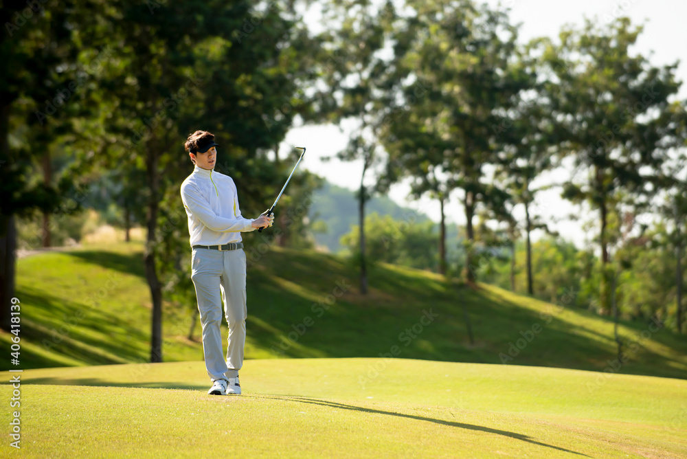 Obraz premium Asian man golfer holding golf club walking on fairway at golf course