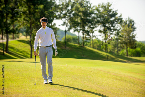 Asian man golfer holding golf club walking on fairway at golf course