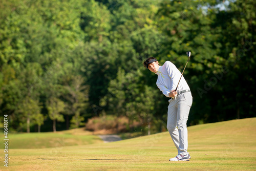 Asian man golfer hitting ball on fairway at golf course