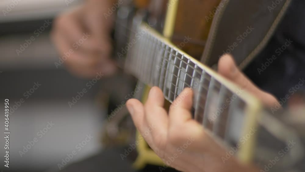 Close up of a professional musician playing a solo on a hollow body electric guitar with a guitar pick during a recording session in a studio with a blurred background. Shot in 4K. Racking Focus.