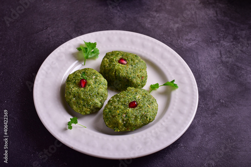 Green pkhali with pomegranate seeds in a white plate on a dark stone table.