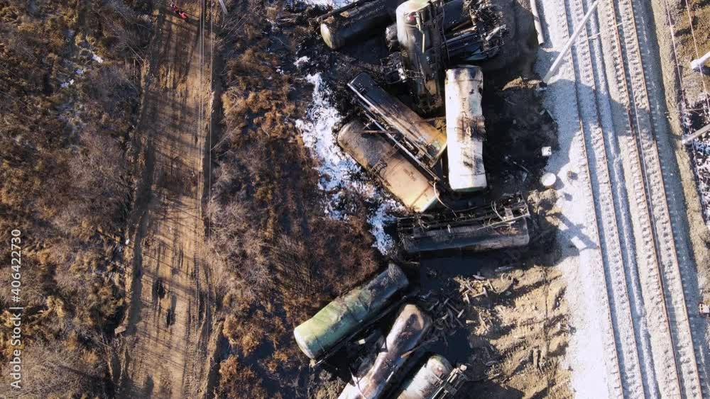 A train wreck on the railroad, scattered tanks, a tractor rides. Aerial view of the accident - a crash with damaged wagons lying next to the rails. Rescuers carry out repair work.