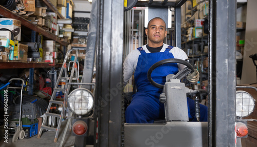 Skilled hispanic worker of building materials warehouse working on forklift truck..