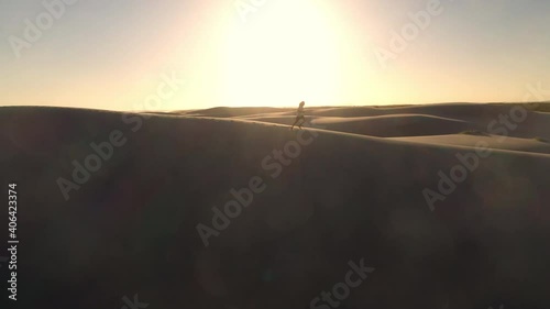 Cinematic drone shot rotating around a silhouetted man running on top of sand dune.  Dark Point sand dunes at Hawks Nest, New South Wales, Australia photo