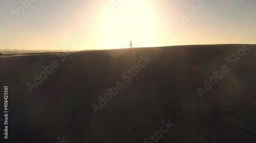 Epic drone shot into the sun revealing a silhouetted man running on top of sand dune.  Dark Point sand dunes at Hawks Nest, New South Wales, Australia photo