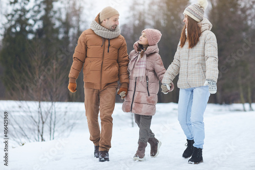 Full length portrait of modern happy family holding hands and smiling while enjoying walk in beautiful Winter forest, copy space