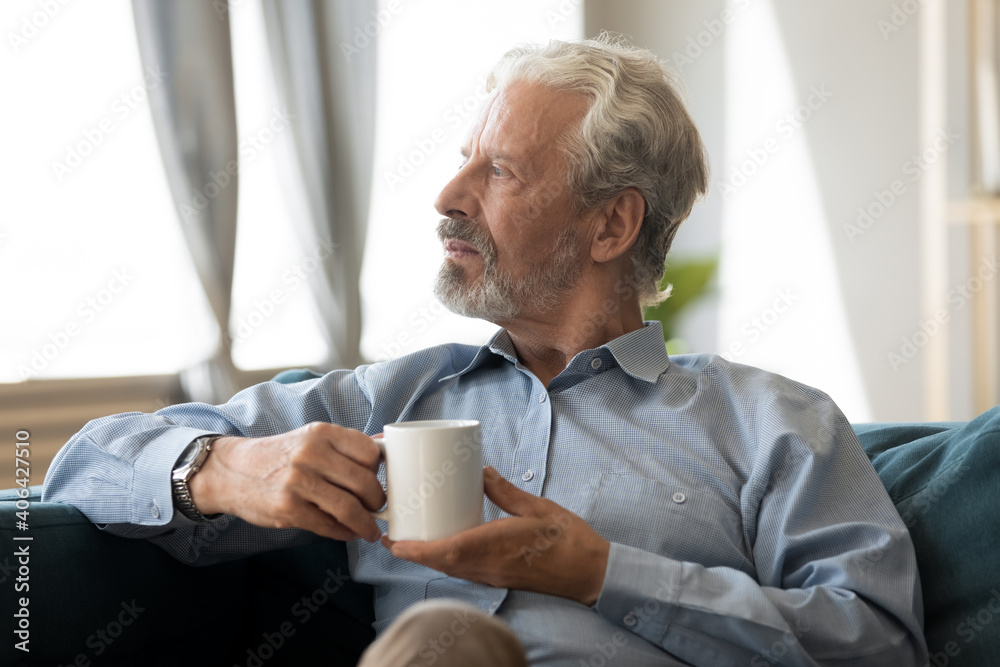 Dreamy inspired older senior hoary man resting on comfortable sofa with hot morning beverage in hands, planning weekend day or enjoying peaceful leisure time alone at home, meditation concept. Dreamy inspired older senior hoary man resting on comfortable sofa with hot morning beverage in hands, planning weekend day or enjoying peaceful leisure time alone at home, meditation concept.