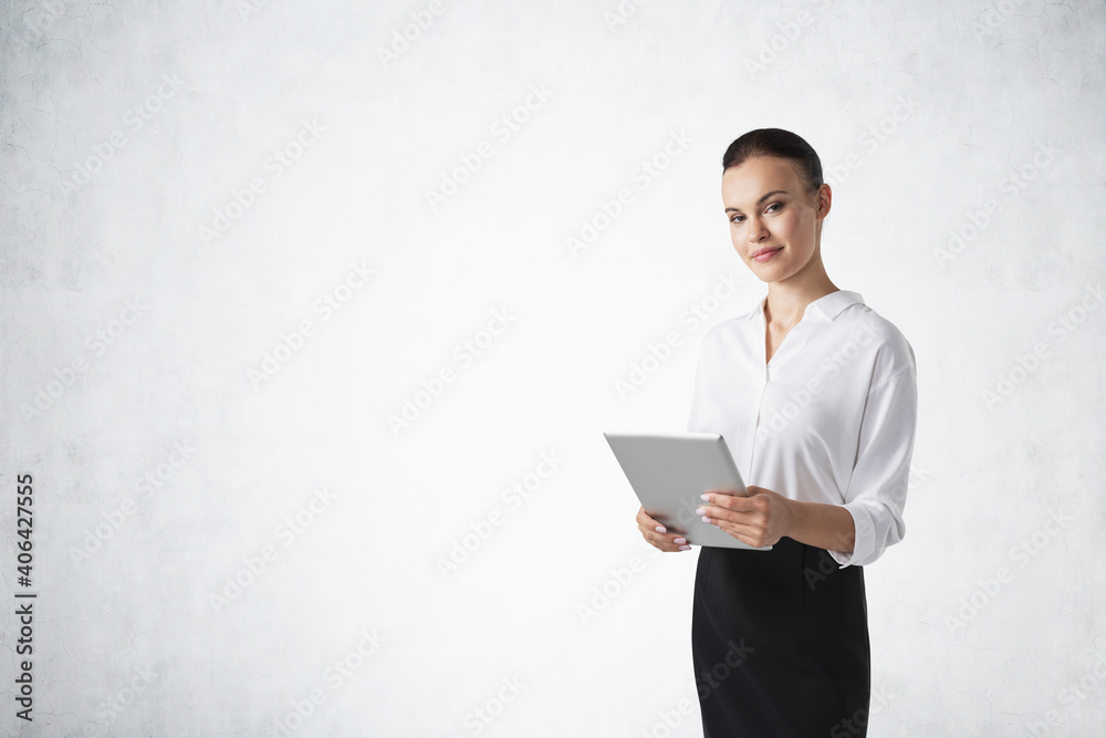 Smiling young businesswoman with tablet standing near concrete wall Smiling young businesswoman with tablet standing near concrete wall
