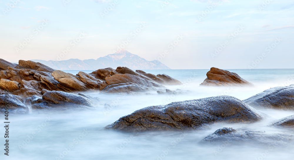 Fototapeta premium Scenic sunset at Sarti beach, Halkidiki, Sithonia, Greece, Europe; view of the fantastic rocky shore with the Mt. Athos in the background; dramatic seascape of the Aegean sea; long exposure shot