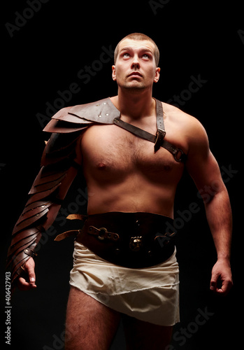 Gladiator with sword and armor on a black background. A warrior in gladiatorial armor looks up at a beam of light