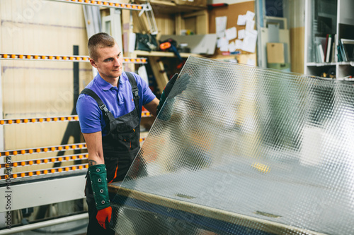 Photos Glazier worker holding a big glass pane in workshop. Industry