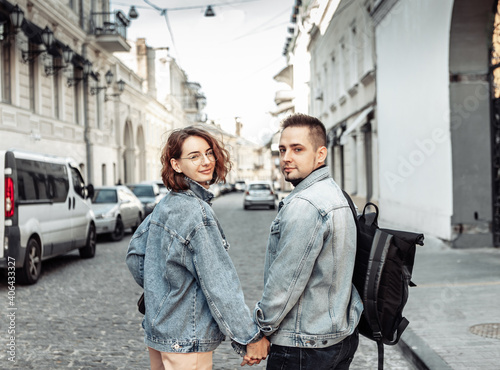 Charismatic modern couple of tourists in love in denim jackets stroll along the urban street