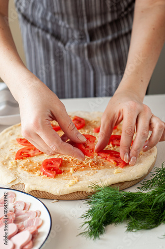 The process of making homemade pizza for Valentine's Day. Women's hands lay the ingredients cut in the form of hearts on the base of the dough.