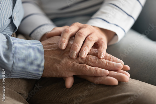 Close up elderly affectionate woman covering wrinkled hands of mature husband  showing love and support at home. Caring middle aged family couple enjoying sincere trustful honest conversation.