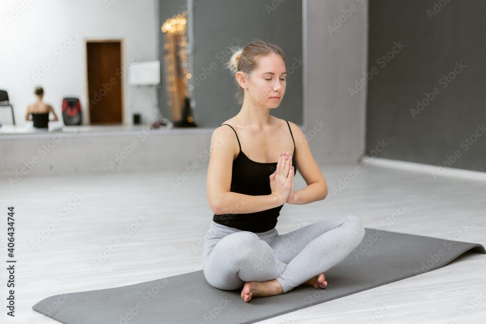 Woman yogi wearing activewear sitting in lotus position folded hands Namaste symbol, do meditation practice during yoga class indoors. No stress improve of self-awareness concept