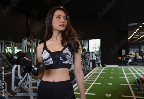 Beautiful asian young woman workout training and exercise with dumbbell weights at fitness gym sport club