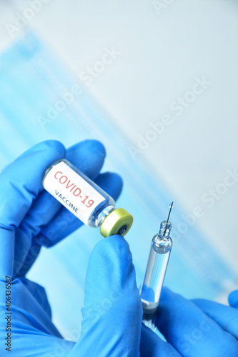 A doctor wearing blue gloves holds a bottle of COVID-19 vaccine.