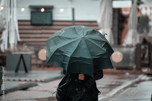 woman walking in the city with green umbrella on rainy and windy day.