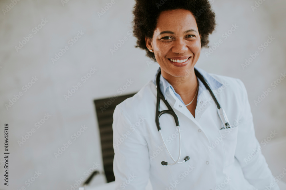 Female African American doctor wearing white coat with stethoscope standing by desk in office Female African American doctor wearing white coat with stethoscope standing by desk in office