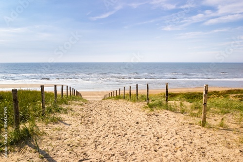 A sandy pathway leading over a levee down to the sea in the netherlands on a bright autumn day