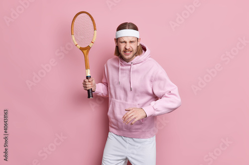 Fototapeta Naklejka Na Ścianę i Meble -  Concentrated tennis player holds racket ready to start game dressed in sportswear doesnt want to defeat prepares for sport competition isolated over pink background. Never give up. Active life