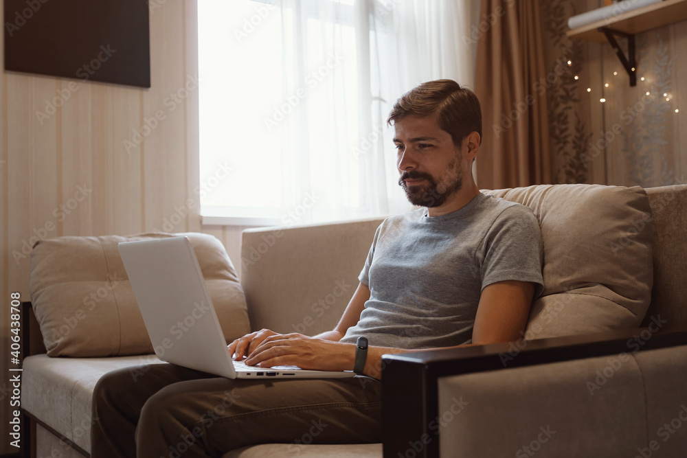 Pensive bearded man sitting on sofa work at laptop
