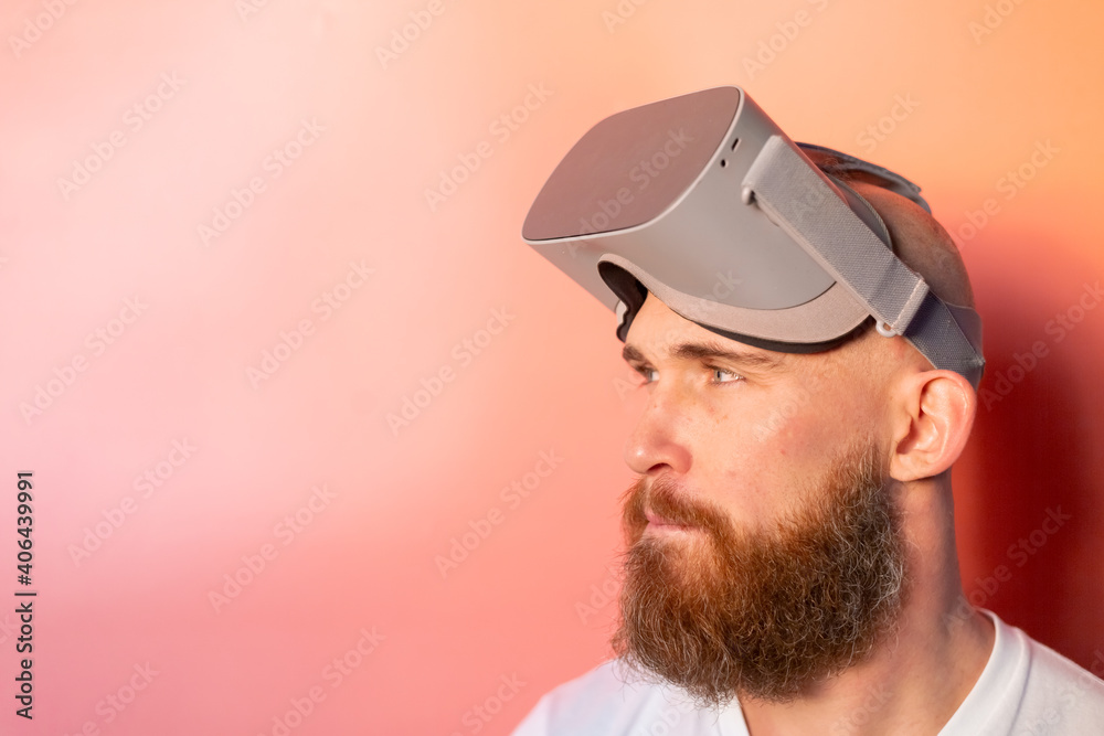 Emotional portrait of a man with a beard wearing virtual reality glasses in the studio on a pink orange background Emotional portrait of a man with a beard wearing virtual reality glasses in the studio on a pink orange background